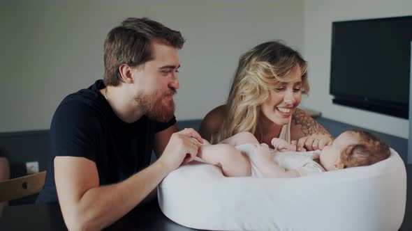 Bearded Handsome Smiling Dad Kissing Leg or Feet of His Newborn Child While Mother Communicate with alt