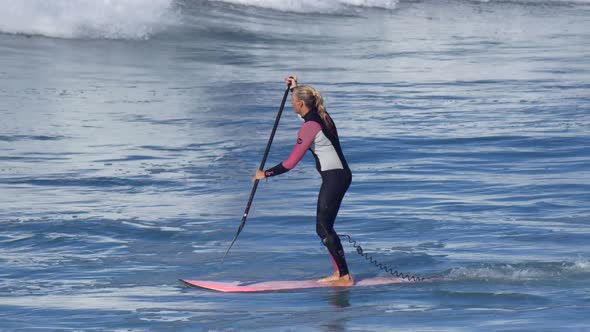 A woman rides an sup stand up paddleboard while surfing on a pink surfboard alt