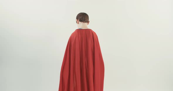 Boy with a superhero cape pretends to fly on a white studio background alt