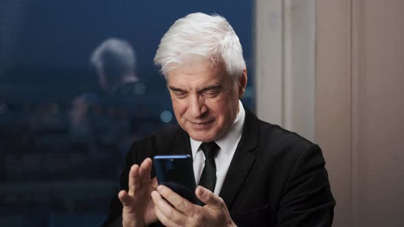 Happy Old Gentleman in Suit with Cellphone Has Distant Conversation and Smiles alt