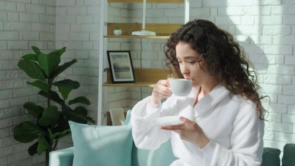 Curly Haired Girl in Bathrobe Looking at Window and Enjoy a Cup of Tea alt