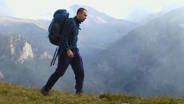 A male hiker in a plaid fleece jacket, standing on the edge of a cliff alt