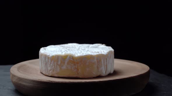 Camembert Cheese Spinning on a Wooden Plate on a Dark Background
