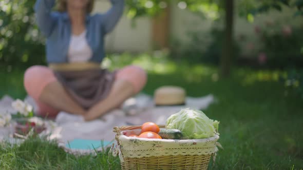 Closeup Basket with Organic Vegetables and Blurred Unrecognizable Senior Woman Meditating in Lotus alt