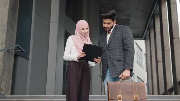 Beautiful Woman in Hijab Holding Clipboard and Showing Some Documents to Muslim alt