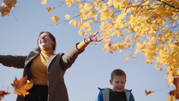 Happy Mom and Son Toss Up Yellow Leaves Against Blue Sky Autumn Yellowed Tree alt