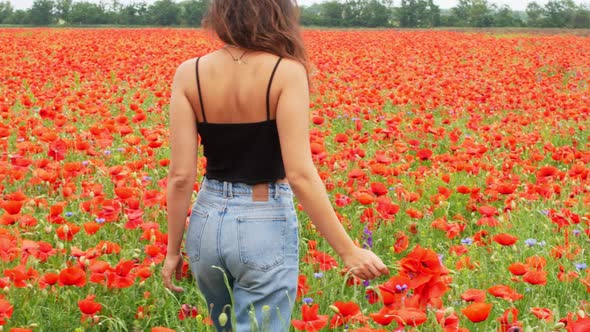 A beautiful young mixed-race woman stands in a field of beautiful red flowers.