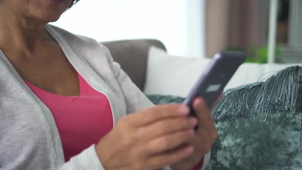 Happy Elderly Woman Holding Smartphone in Hand, Watching Screen in Home Room alt