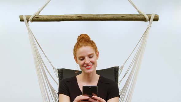 Businesswoman using mobile phone while relaxing on a hammock alt