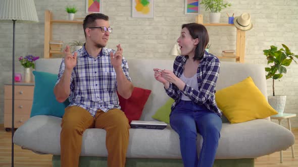 Young Married Couple Sitting in the Living Room Rejoices in a Positive Pregnancy Test alt
