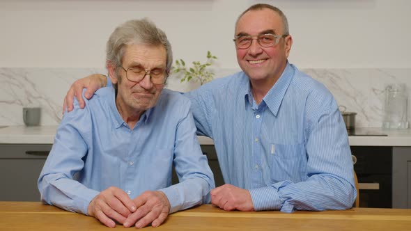 Portrait of the Two Caucasian Old Men Sitting Hugging and Smiling to the Camera in Front of the alt