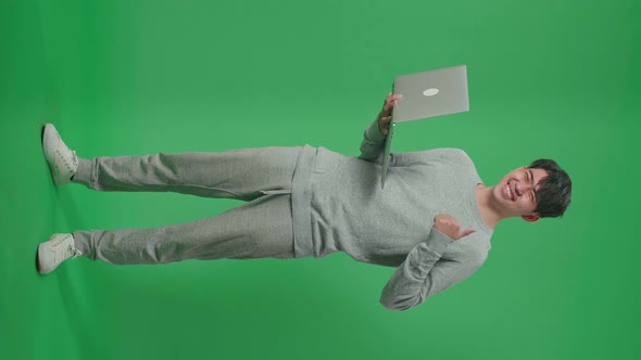 Full Body Of Smiling Asian Man Showing Thumbs Up Gesture While Typing On Computer On Green Screen alt