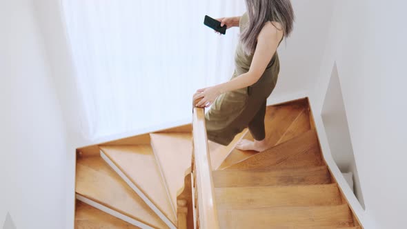 Asian woman walking on the stairs and looking at the phone alt