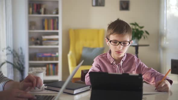 Boy Son Doing Homework From Distant Learning at Home While Mother is Telecommuting alt
