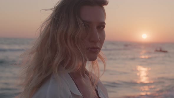 Young Blonde Woman with Wavy Hair Standing on Beach By the Sea on Sunset