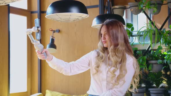 Beautiful Woman Standing with Selfie Stick in Cafe alt