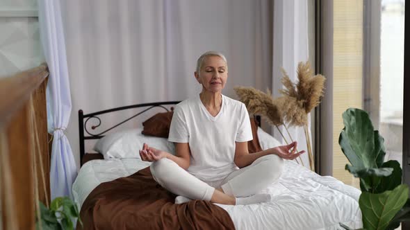Senior Woman Practicing Yoga in Lotus Positionitting at Bedroom