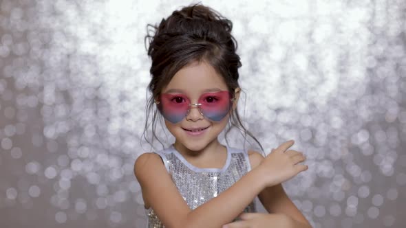 Cute Happy Little Girl Child in a Silver Dress Dancing on Background of Silver Bokeh