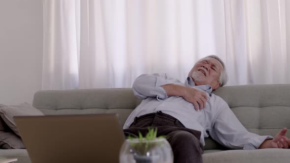Asian Elderly man Chest pain due to heart disease on the sofa in the living room. alt