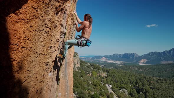 Strong and Muscular Fit Rock Climber Climbs By Rope on Vertical Cliff alt
