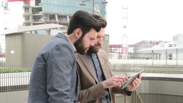 Two young bearded men outdoor discussing using digital tablet alt