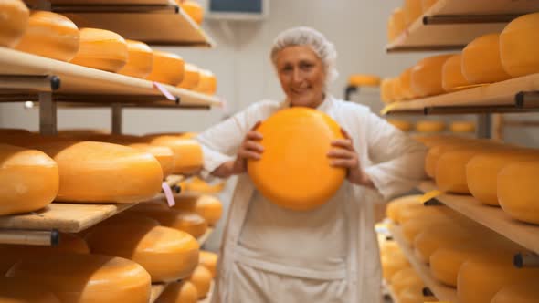 Smiling female worker holding wheel of cheese in storage