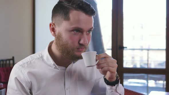 Young Attractive Man Sitting in Cafe and Drinking Coffee Slow Motion alt