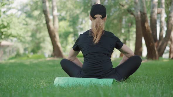 Back View of Mid-adult Sportswoman Sitting on Exercise Mat and Breathing. Female Caucasian Yogi alt