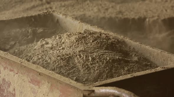 worker pours sand into a concrete mixer with shovel