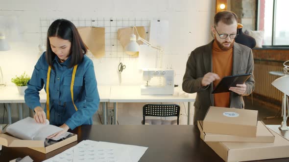 Tailoring Studio Employee Packing Clothes While Business Owner Checking Orders Using Tablet alt