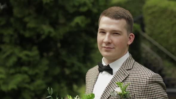 Groom, Young Man in the Green Summer Park with a Wedding Bouquet. He Waiting for His Beloved Bride alt