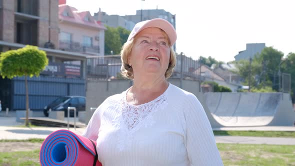 Smiling elderly sports woman confidently walks in the morning park alt