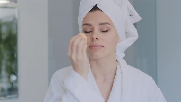 Attractive young brunette Woman in bathrobe  applying foundation with beauty blender alt