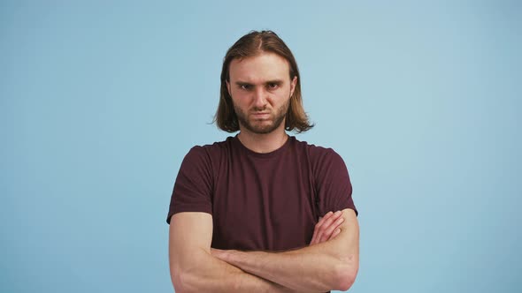Young Longhaired Man Has Folded His Hands Grimacing and Looking Offended or Upset While Posing on alt