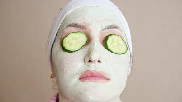 Woman Sitting with a Mask on Face and Cucumber Rings Over Eyes alt