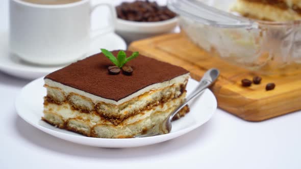 Traditional Italian Tiramisu dessert in glass baking dish, portion on plate and cup of coffee alt