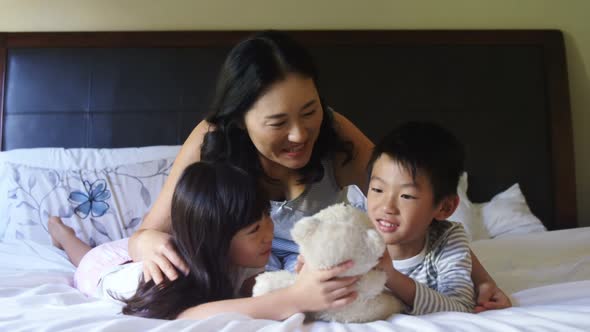 Mother and kids playing with teddy bear in bedroom alt