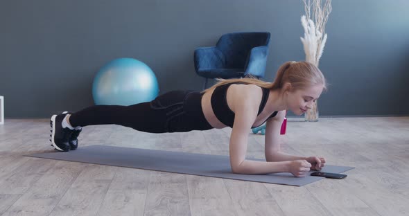 Strong Girl Doing Plank , Using Stopwatch on Her Phone alt