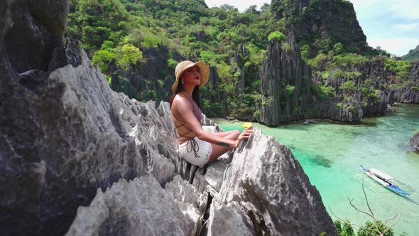 Woman In Sun Hat Sitting On Rocks Above Hidden Beach alt
