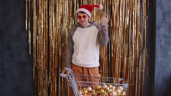 Male with Shopping Cart Filled of Assorted Baubles Near Wall with Golden Tinsel alt