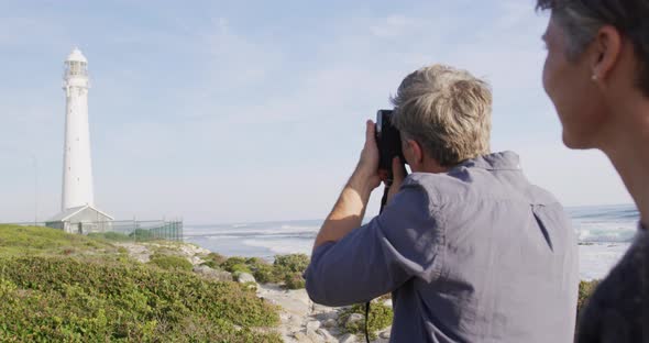 Caucasian couple enjoying free time by sea on sunny day taking photo with camera alt