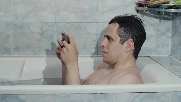 Man Playing Game on Smartphone in a Bathtub alt