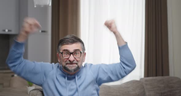 Man Sitting at Home on the Couch Joy of Happiness Good News Rejoices in Winning the Game Gestures alt