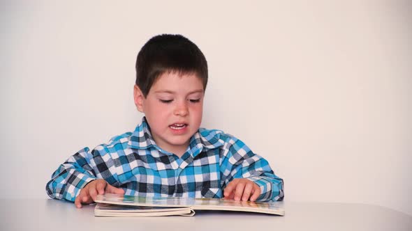 A 4Yearold Boy Looks at a Book with Thick Cardboard Pages with Pictures alt