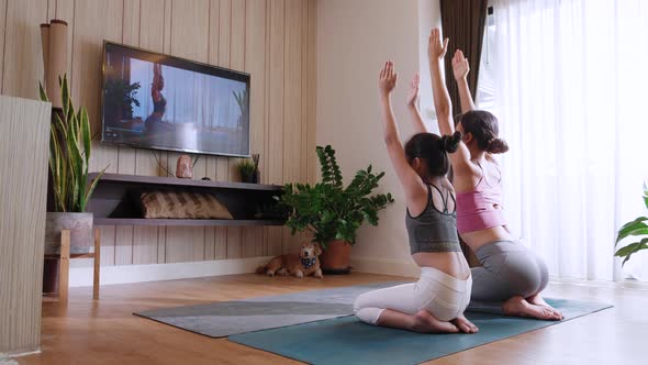 Young woman and little daughter practicing yoga and watching live or video practice TV online