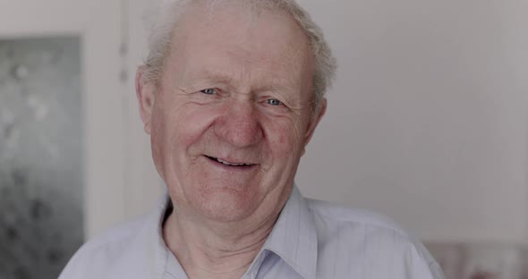 Portrait of Happy Senior Man Smiling and Talking at Camera in Light Room alt