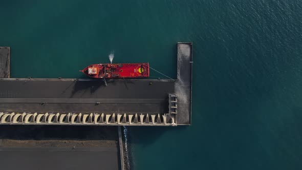 Red cargo ship anchored at quay of Tazacorte harbor in La Palma island. Aerial top-down sideways alt