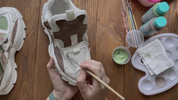 Girl's Hands Paint Sneakers with Brush on Wooden Table