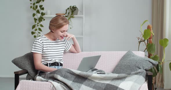 Caucasian Woman Sitting on Sofa at Home Under Blanket Finishes Conversation on Video Chat Online alt