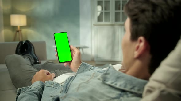 Back View of Brunette Man Holding Chroma Key Green Screen Smartphone Watching Content Without
